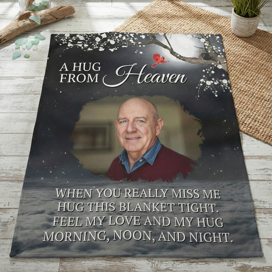 Memorial blanket with photo of a man and text 'A Hug from Heaven' on a wooden surface.